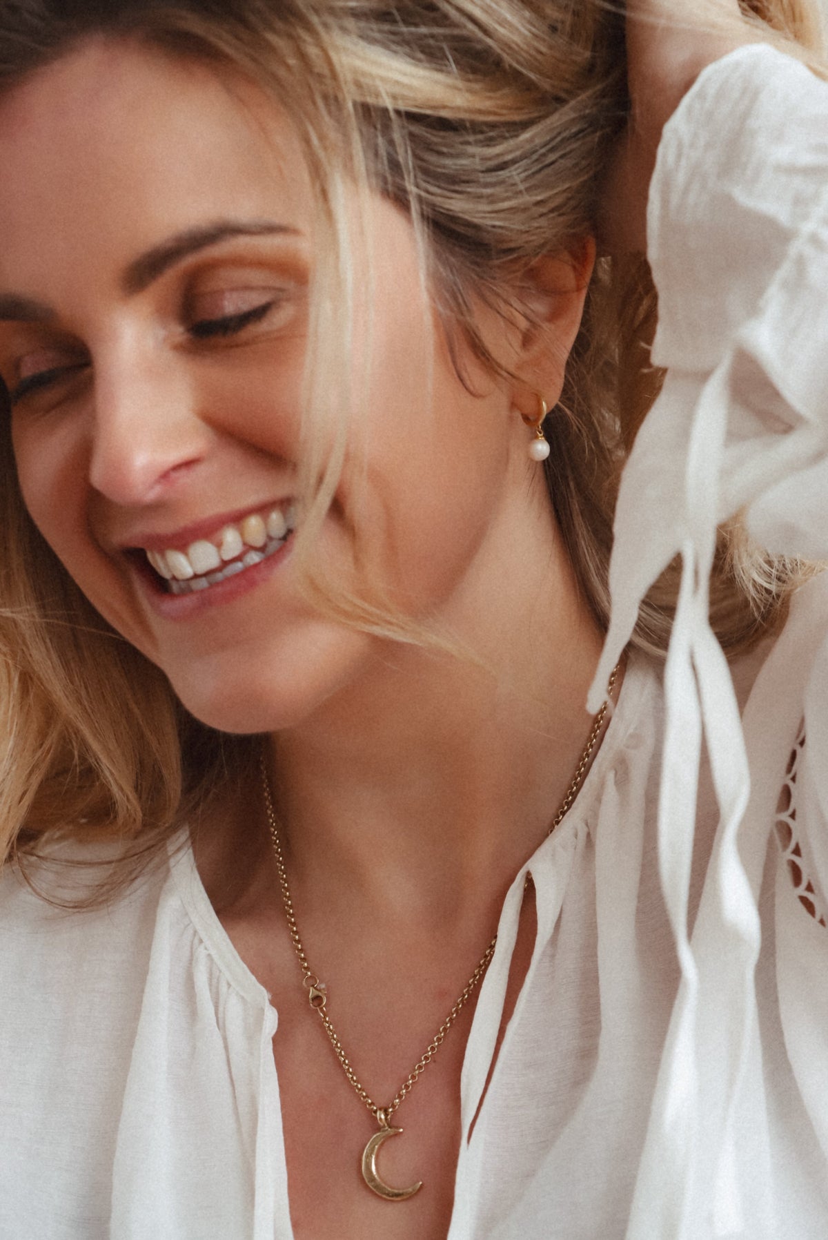 Model wearing 14ct gold-plated pearl huggie hoops with a white blouse and crescent moon necklace