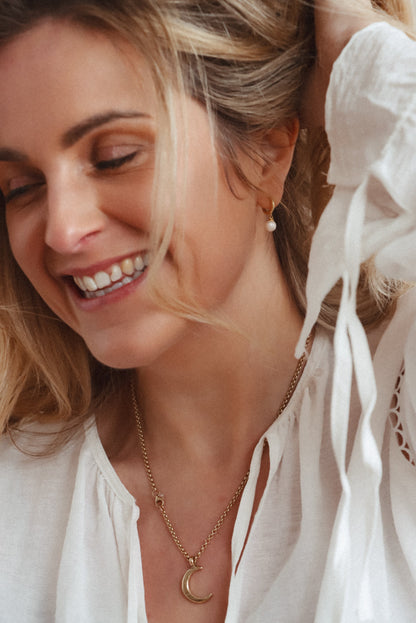 Model wearing 14ct gold-plated pearl huggie hoops with a white blouse and crescent moon necklace