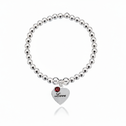 Silver beaded bracelet with a heart-shaped tag and red gemstone on a white background