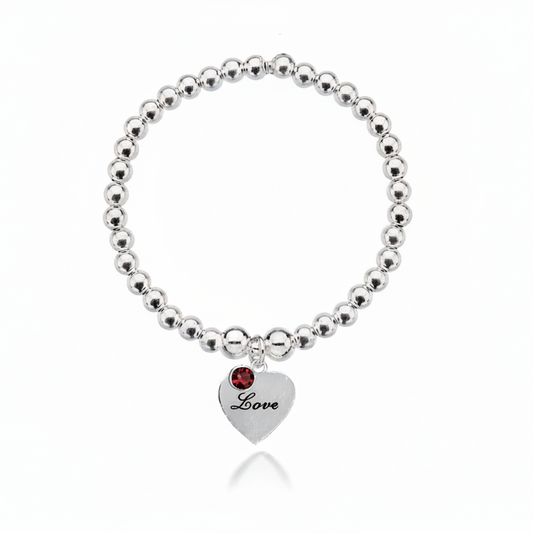 Silver beaded bracelet with a heart-shaped tag and red gemstone on a white background