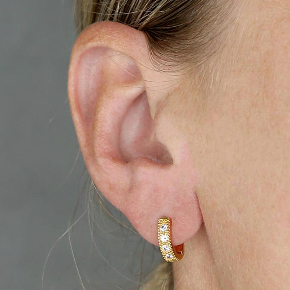 14ct gold-plated horseshoe hoop earring with sparkling clear stones and beaded edging, worn on an earlobe