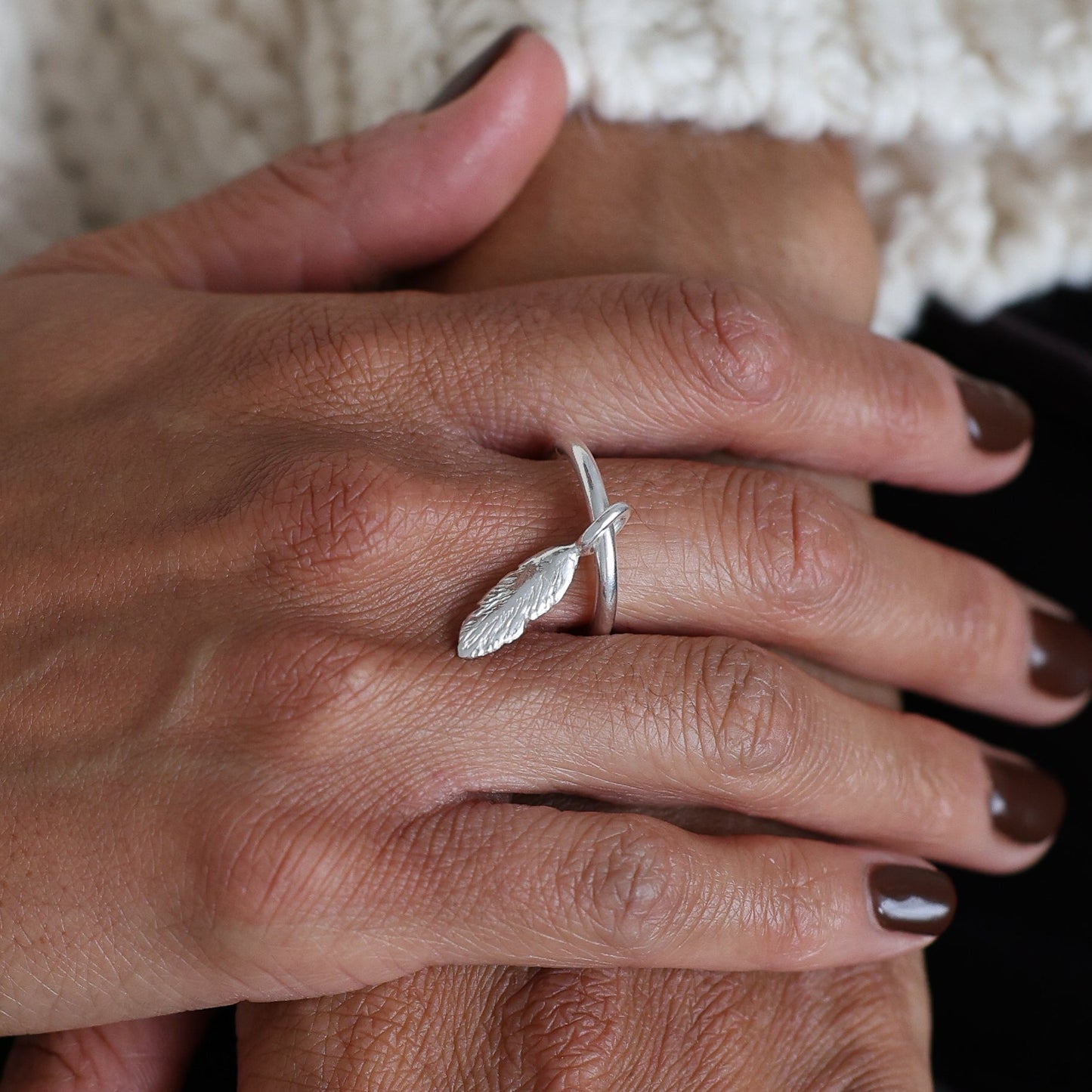 Close-up of hands with rings wearing a white sweater and black pants.