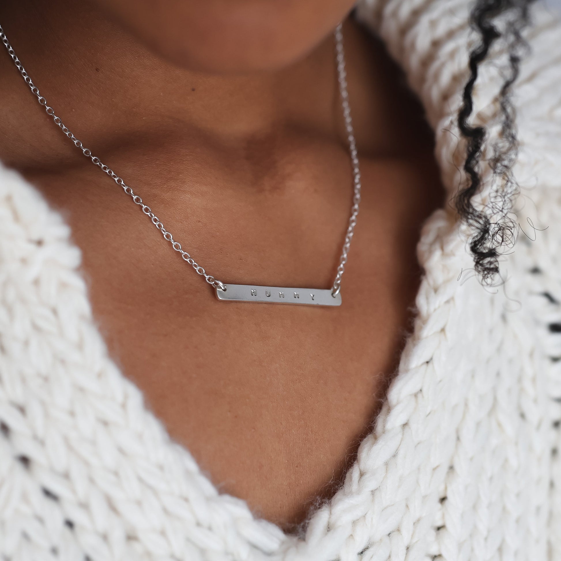 Person wearing a white knitted sweater and a silver necklace with a bar pendant.