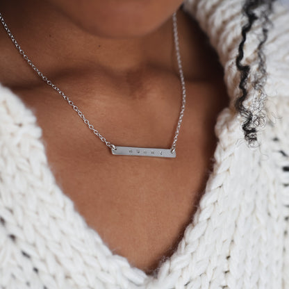 Person wearing a white knitted sweater and a silver necklace with a bar pendant.