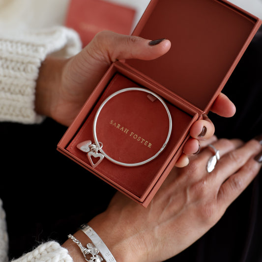 Person holding a red jewelry box with a silver bracelet inside, wearing a white sweater.
