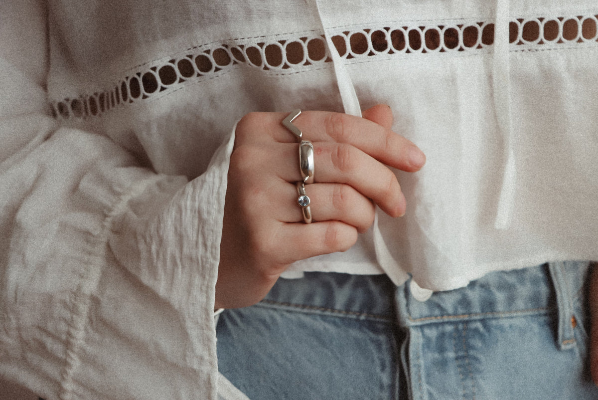 Sterling silver Lava Ring worn alongside a V-shaped ring and a gemstone ring, with a white blouse and blue jeans