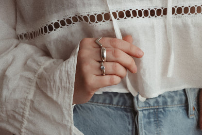 Sterling silver Lava Ring worn alongside a V-shaped ring and a gemstone ring, with a white blouse and blue jeans