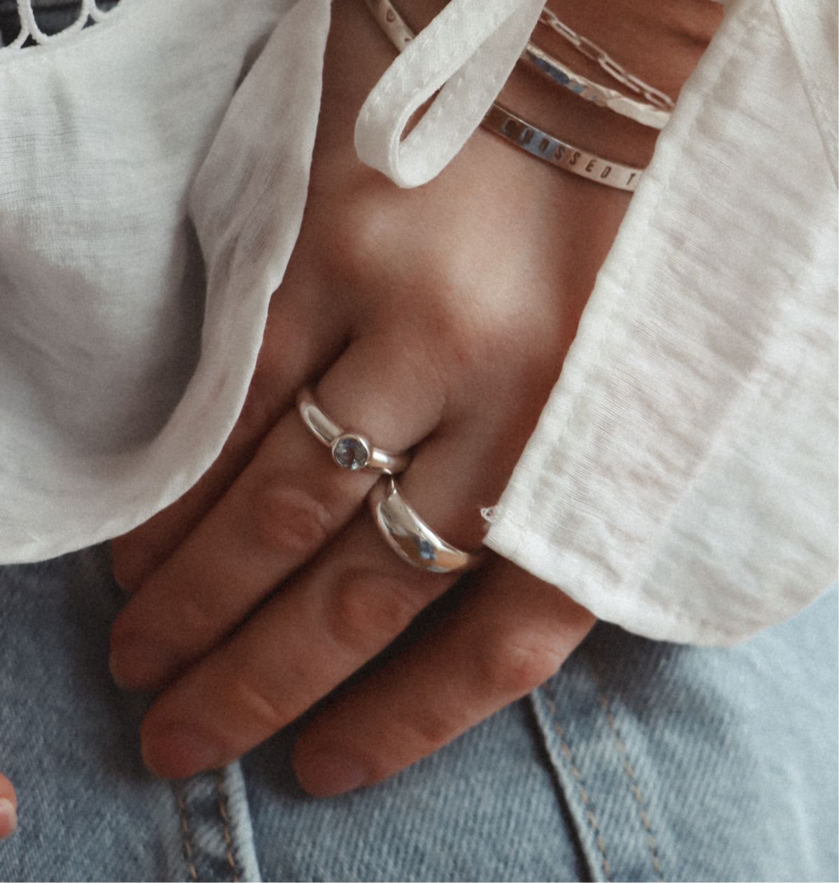 Sterling silver Lava Ring with an organic textured band, worn beside a gemstone ring with a white blouse and jeans