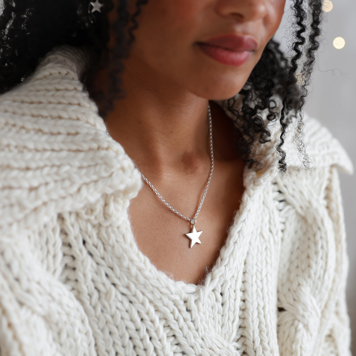 silver star necklace worn by a model in a white knitted sweater 