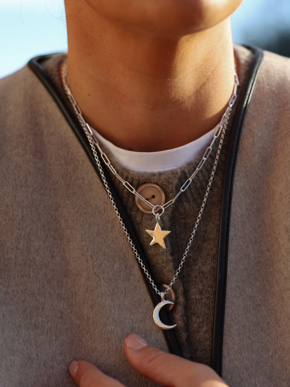 Person wearing a necklace with star and moon pendants on a blurred background