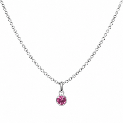 A delicate silver chain necklace with a small round bezel-set pink gemstone pendant, displayed against a solid white background.