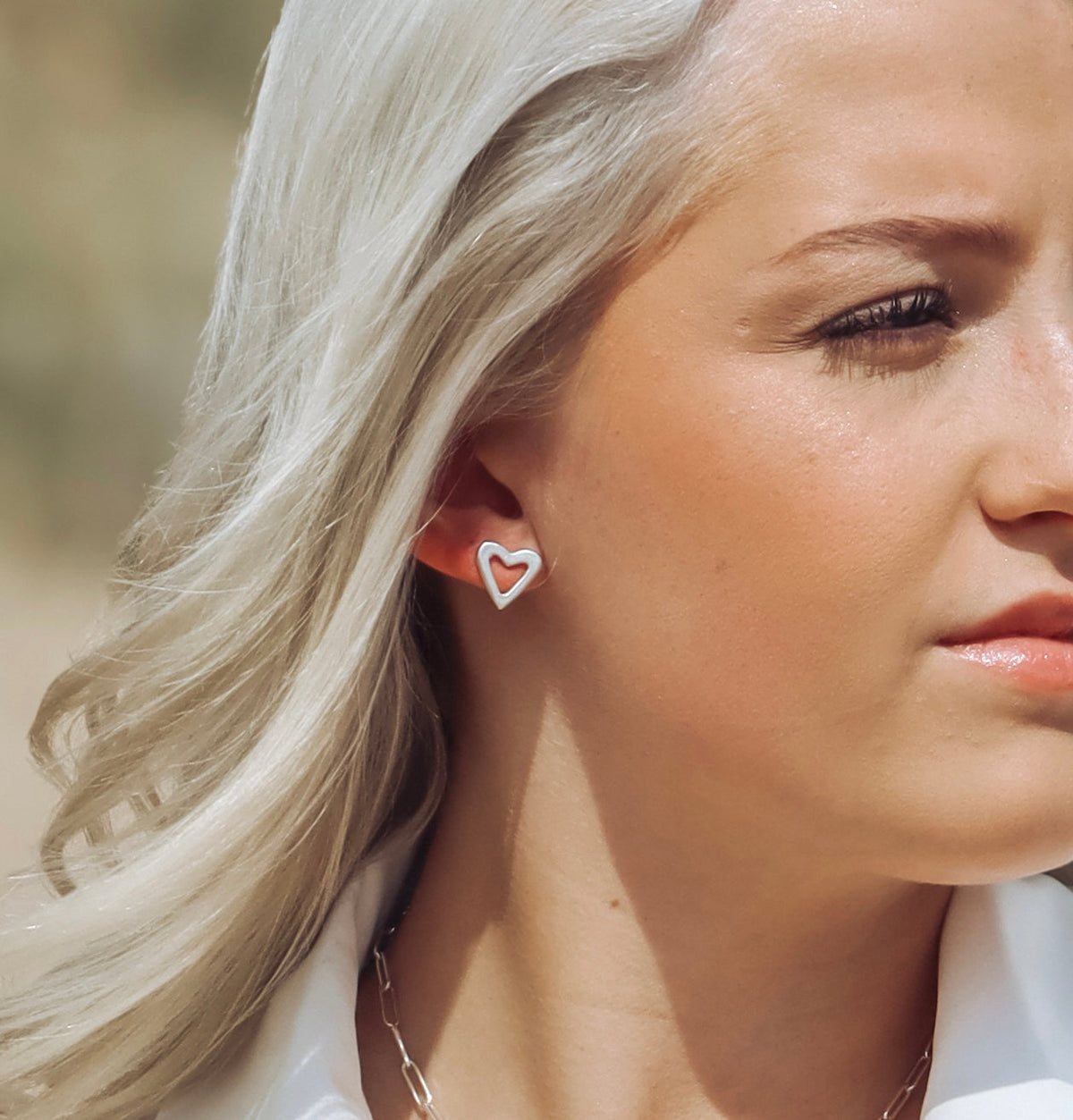Handmade sterling silver open-heart stud earrings with a hammered finish worn in a ear