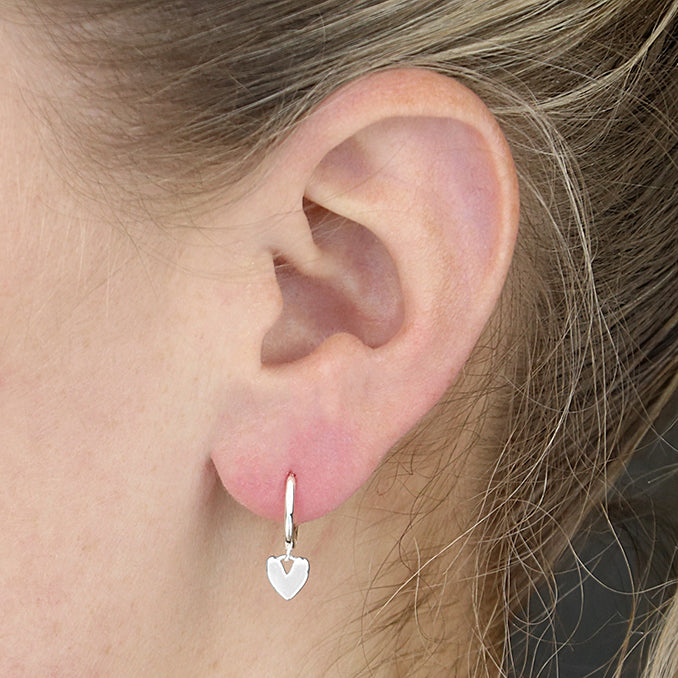 Close-up of an ear wearing a silver hoop earring with a heart charm.