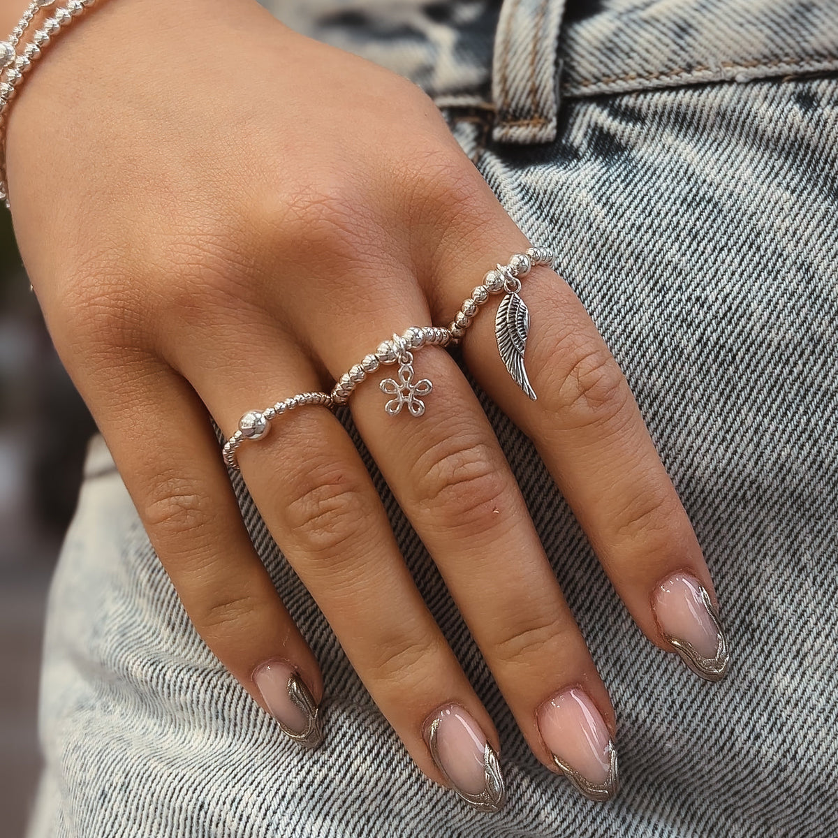 Sterling silver beaded rings, including flower and wing charms, worn on a hand resting on denim