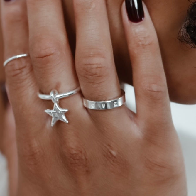 close up of a Hand-stamped sterling silver Signature Quote Band Ring paired with a star dangle ring 