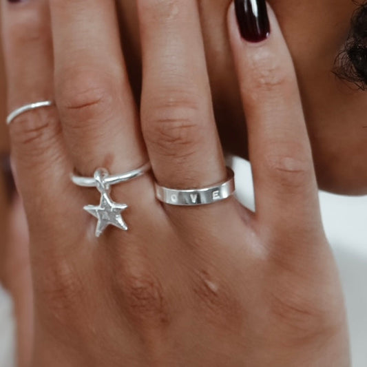 close up of a Hand-stamped sterling silver Signature Quote Band Ring paired with a star dangle ring 