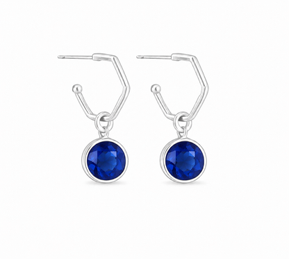 A pair of silver hoop earrings featuring sapphie charms shown on a plain white background.