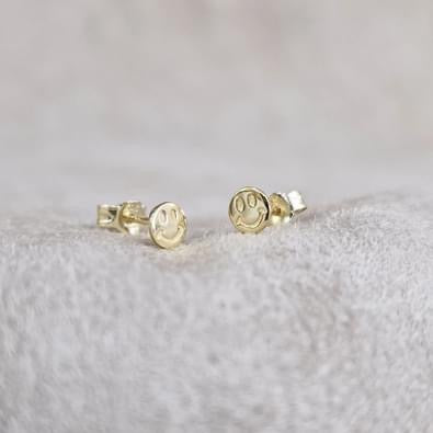 Pair of 14ct gold-plated smiley face stud earrings with butterfly backs on a pale textured surface