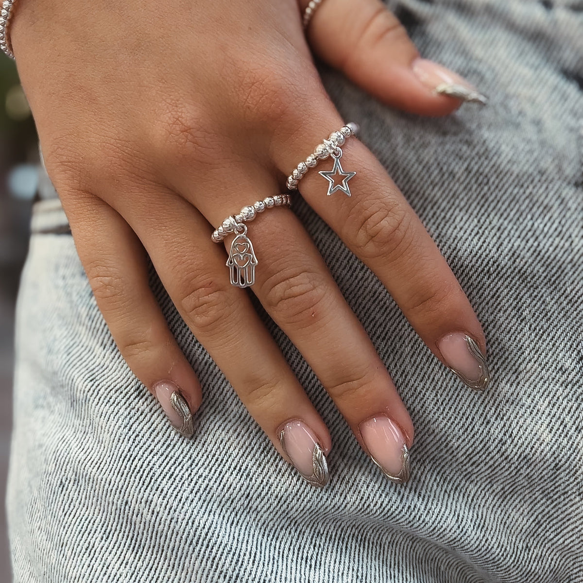 terling silver beaded rings with open star and Hamsa hand charms, worn on a hand resting on denim