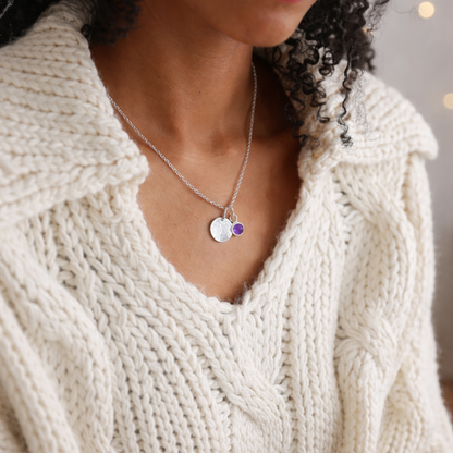 Sterling silver Tanzanite Talisman Necklace with a round disc and purple gemstone charm, worn with white knitwear