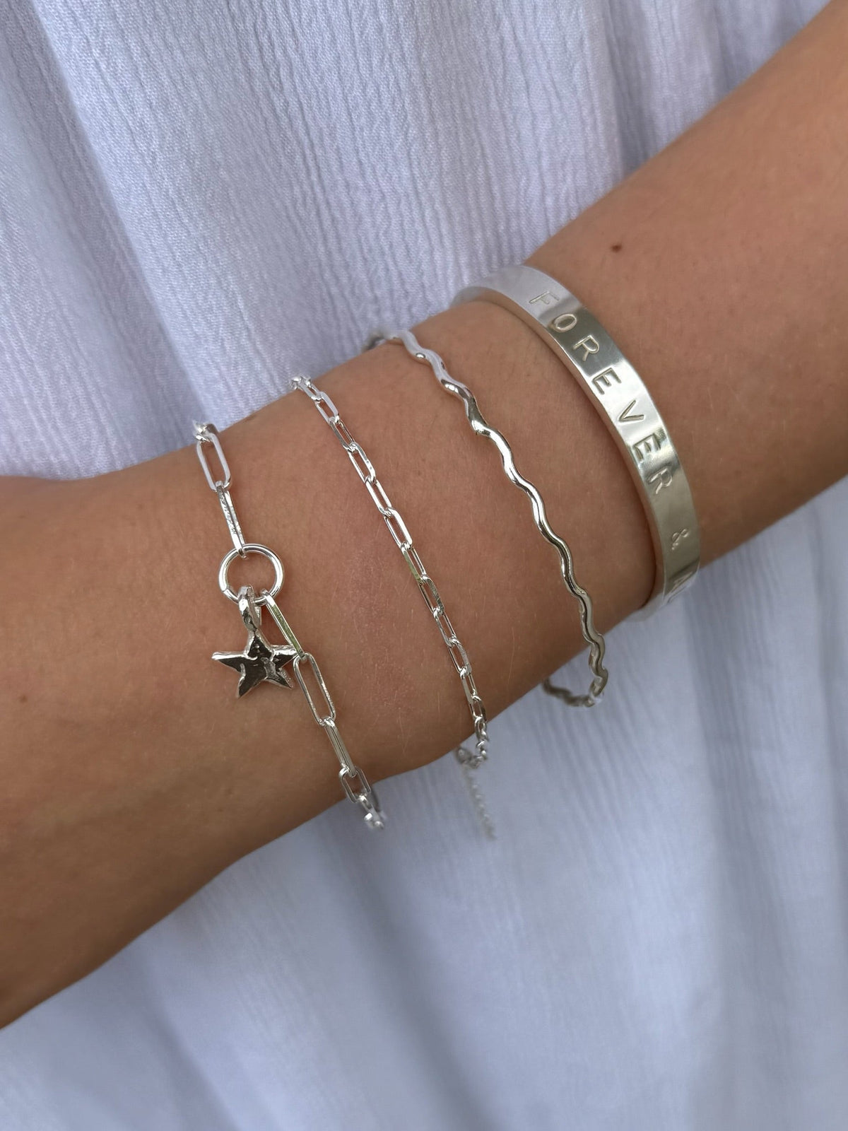 sterling silver Teeny Trace Bracelet worn alongside a star charm bracelet, wavy bangle and engraved silver cuff.