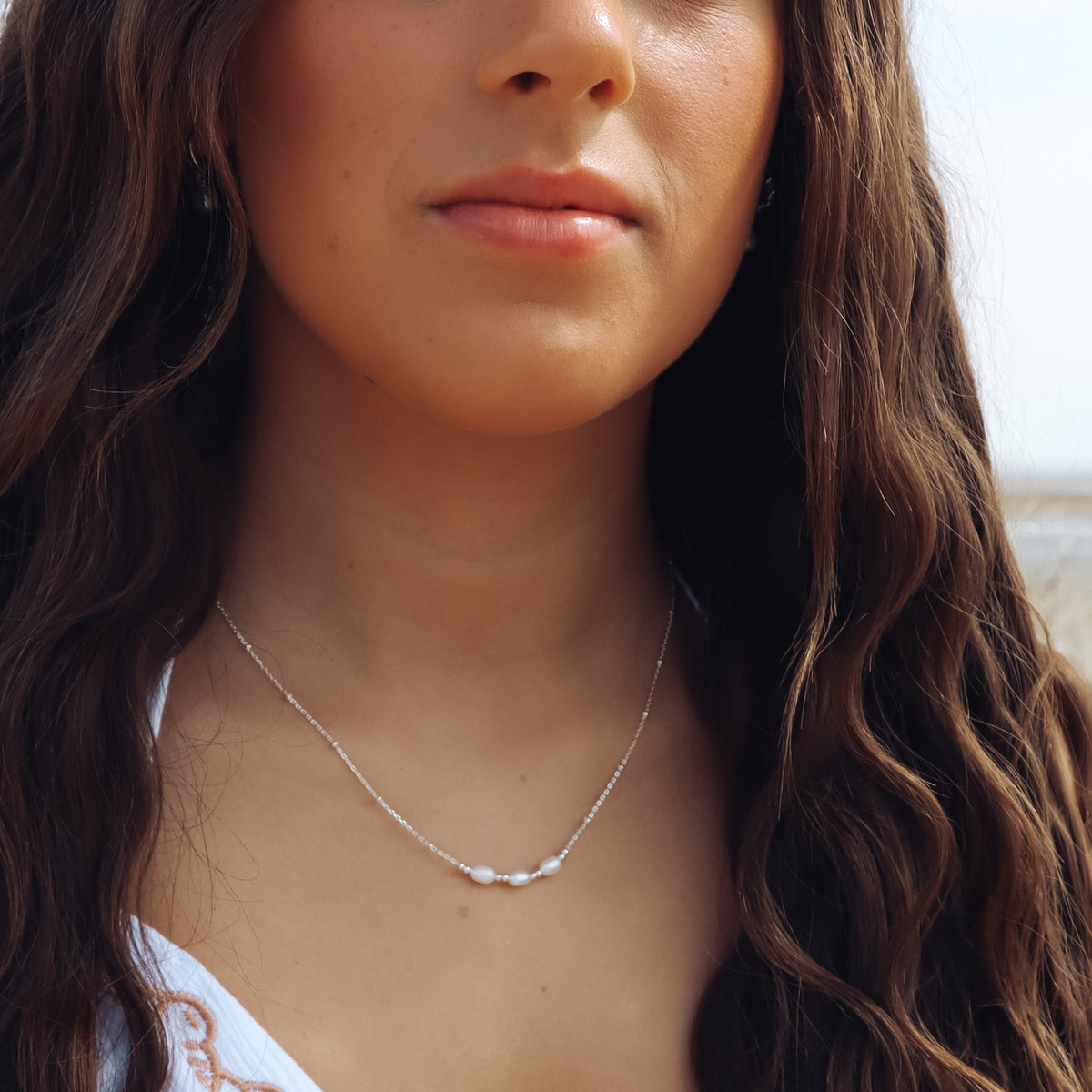 Close-up of a woman wearing a delicate triple pearl necklace with a blurred background