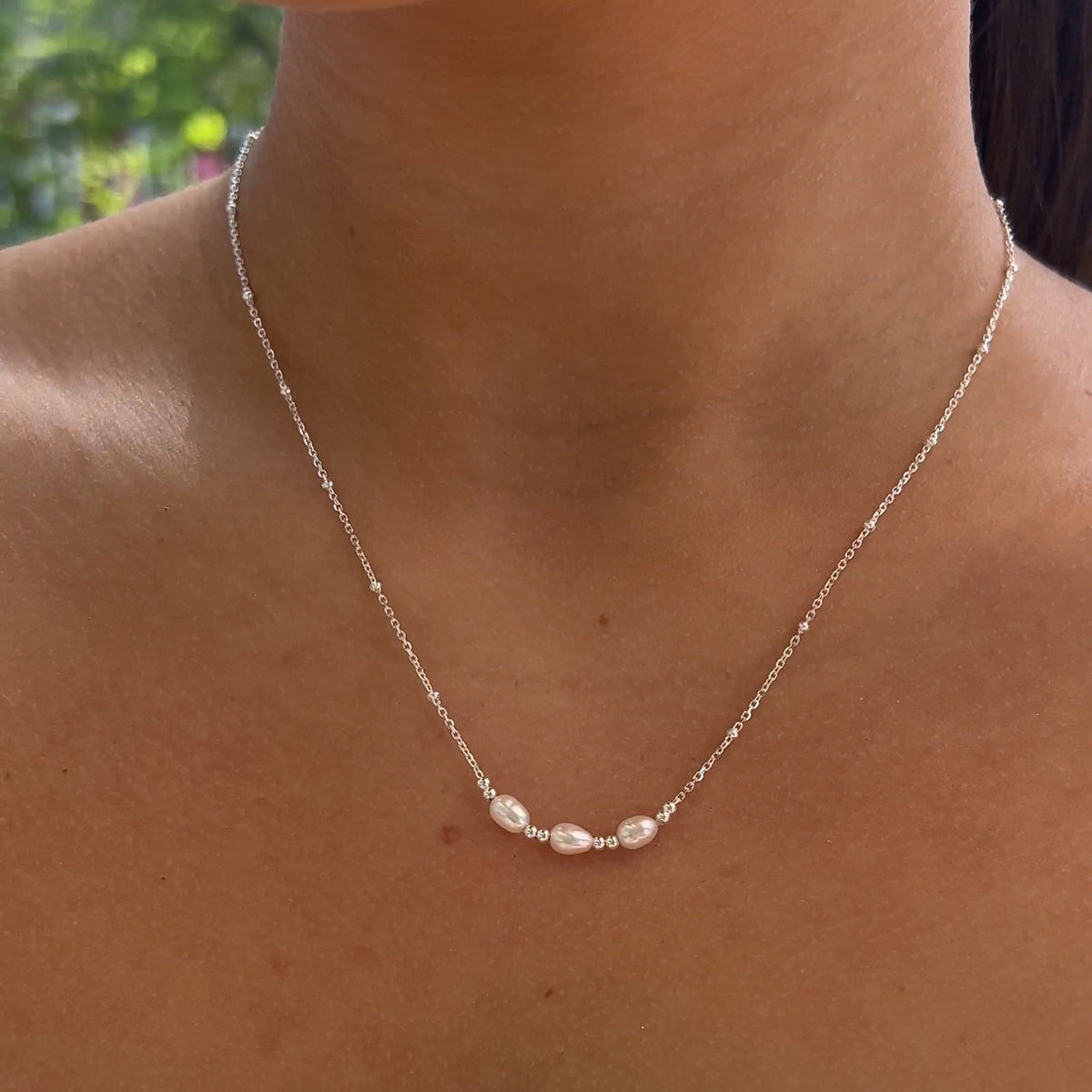 Silver necklace with small pearls on a person's neck against a blurred background
