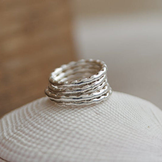 Sterling silver Wave Stacking Rings with textured wavy bands, stacked on a white shell
